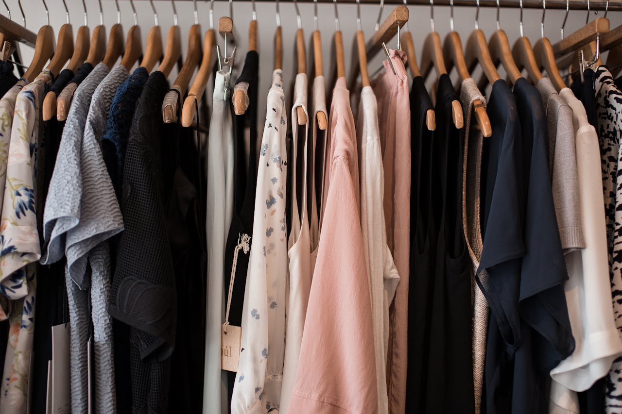gallery-3 A stylish collection of women's clothing hanging on wooden hangers in a boutique setting.